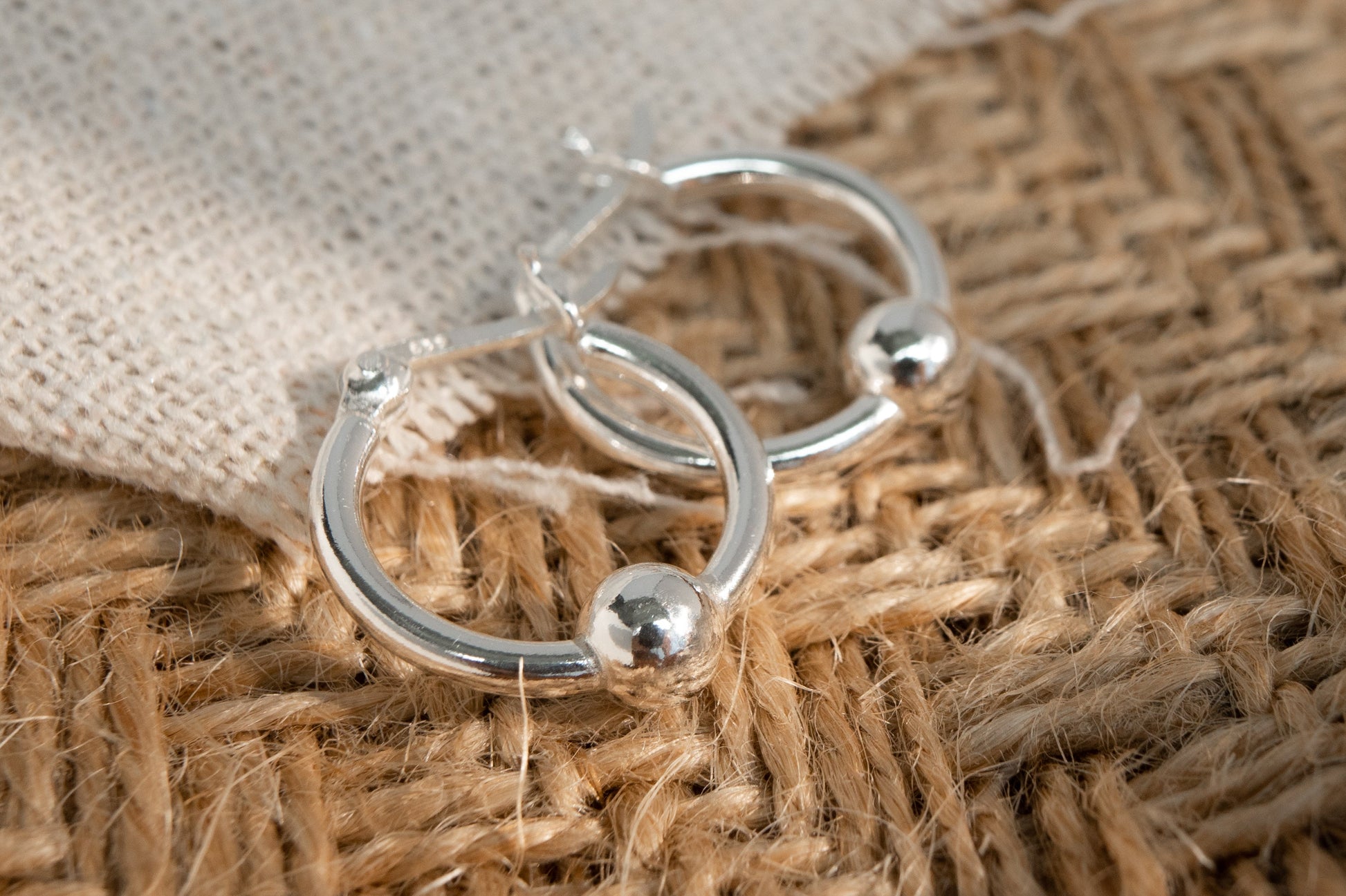 Silver hoop earrings on a textured brown fabric background