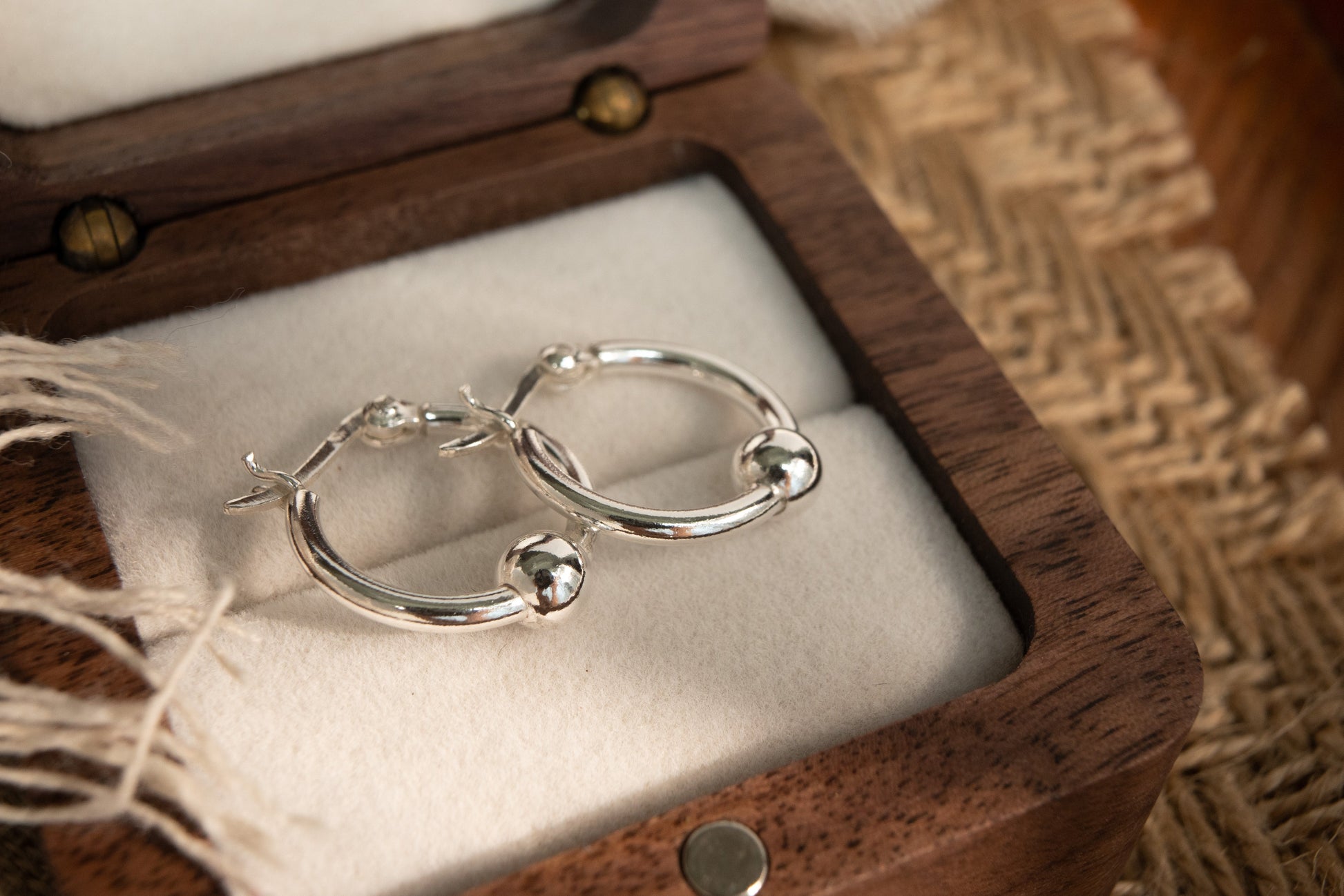 Silver hoop earrings in a wooden jewelry box on a textured surface