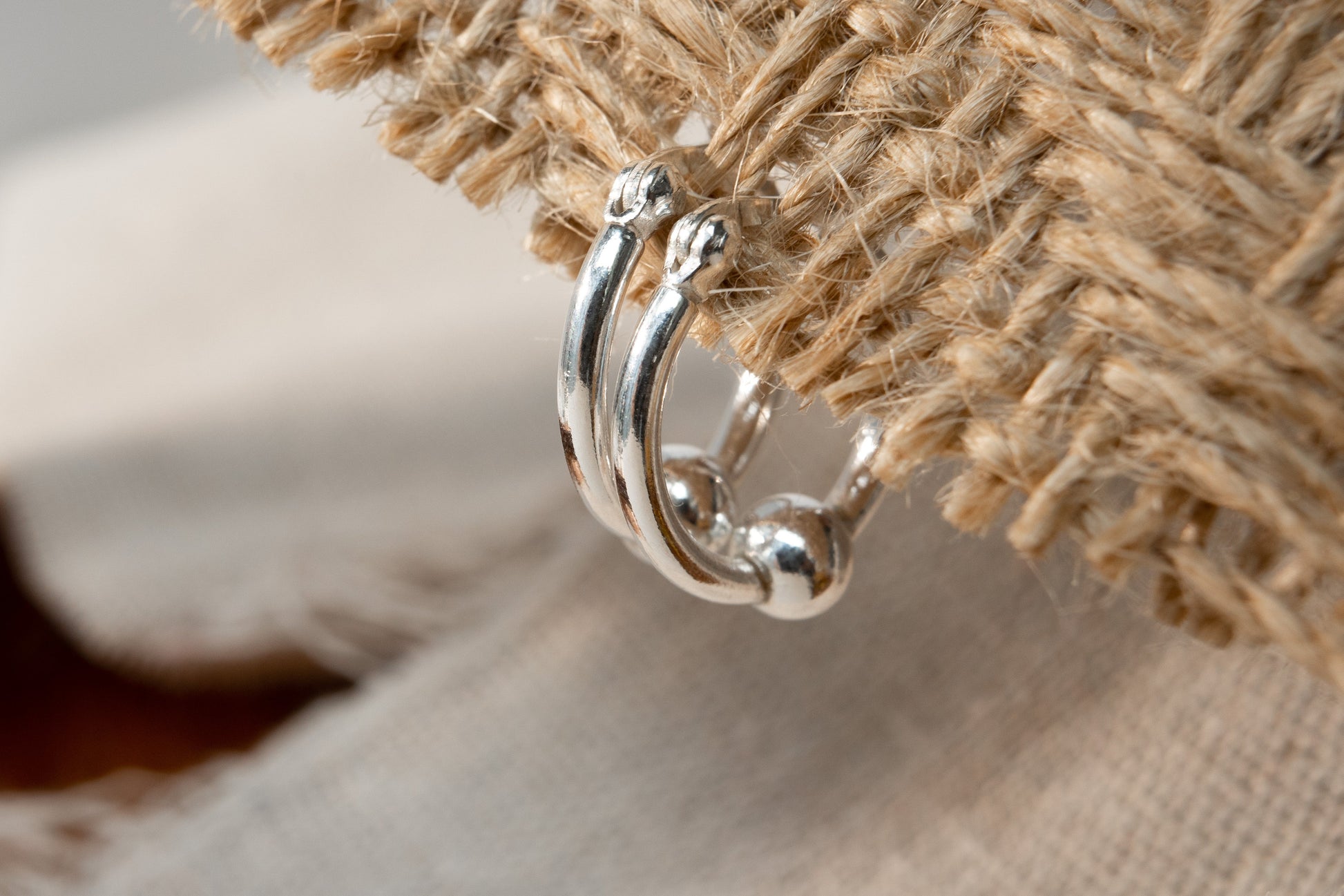 Silver hoop earring on a textured beige fabric background