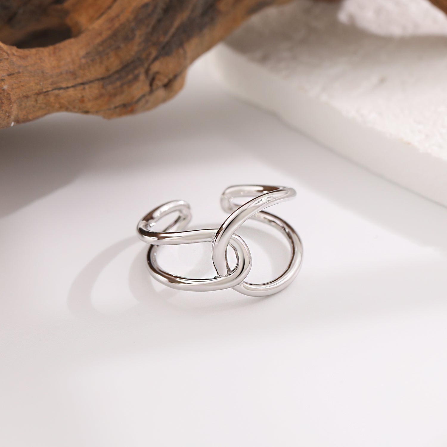 Silver ring on a white surface with a natural wood piece in the background