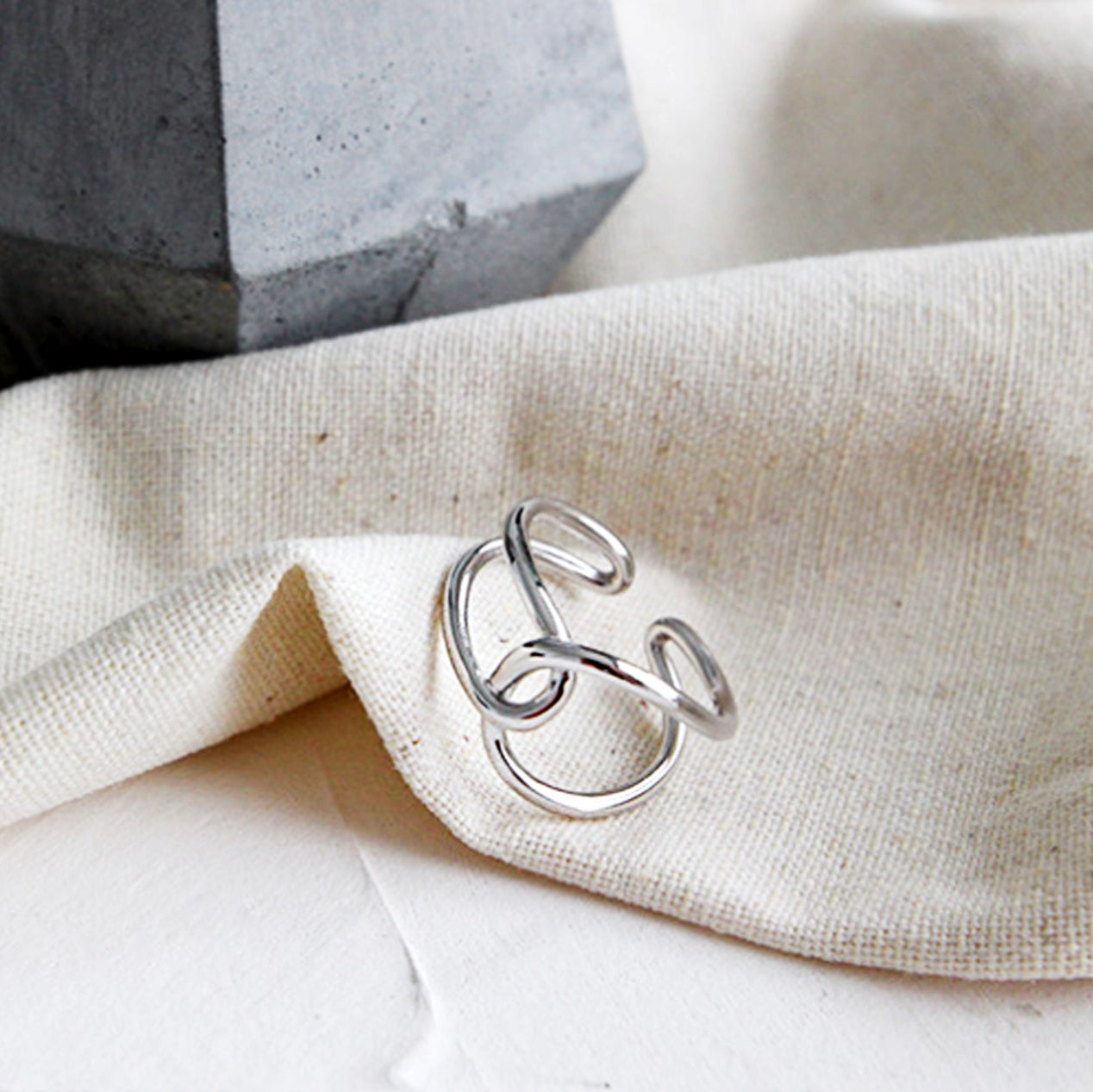 Silver ring on a beige fabric surface with a gray stone object in the background