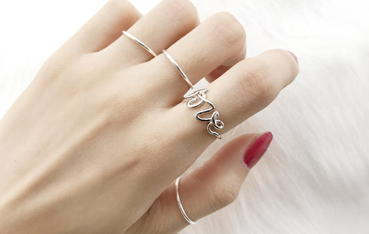 Hand wearing two silver rings with 'love' engraving on a white background