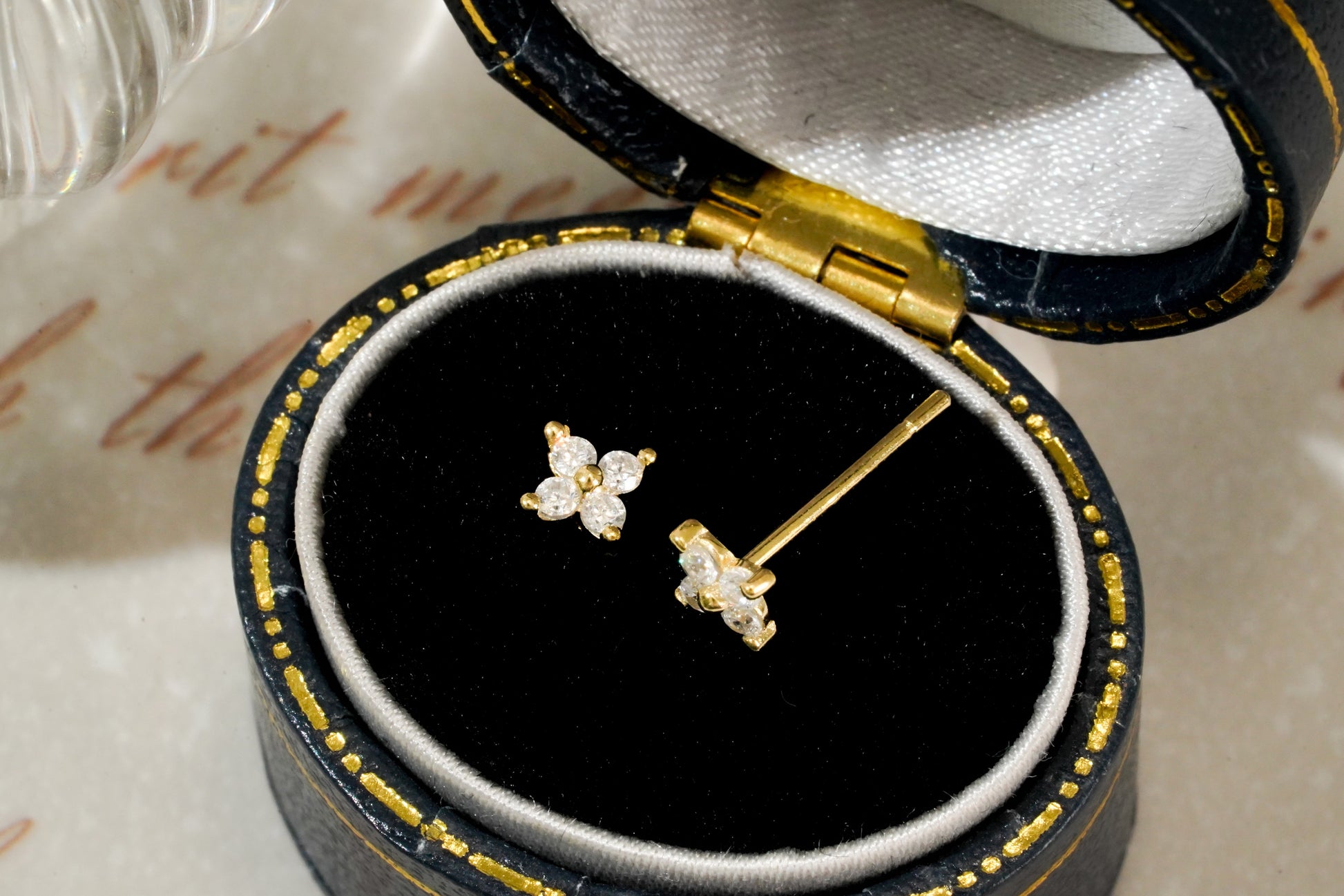 Gold earrings with floral designs in a black jewelry box on a textured surface.