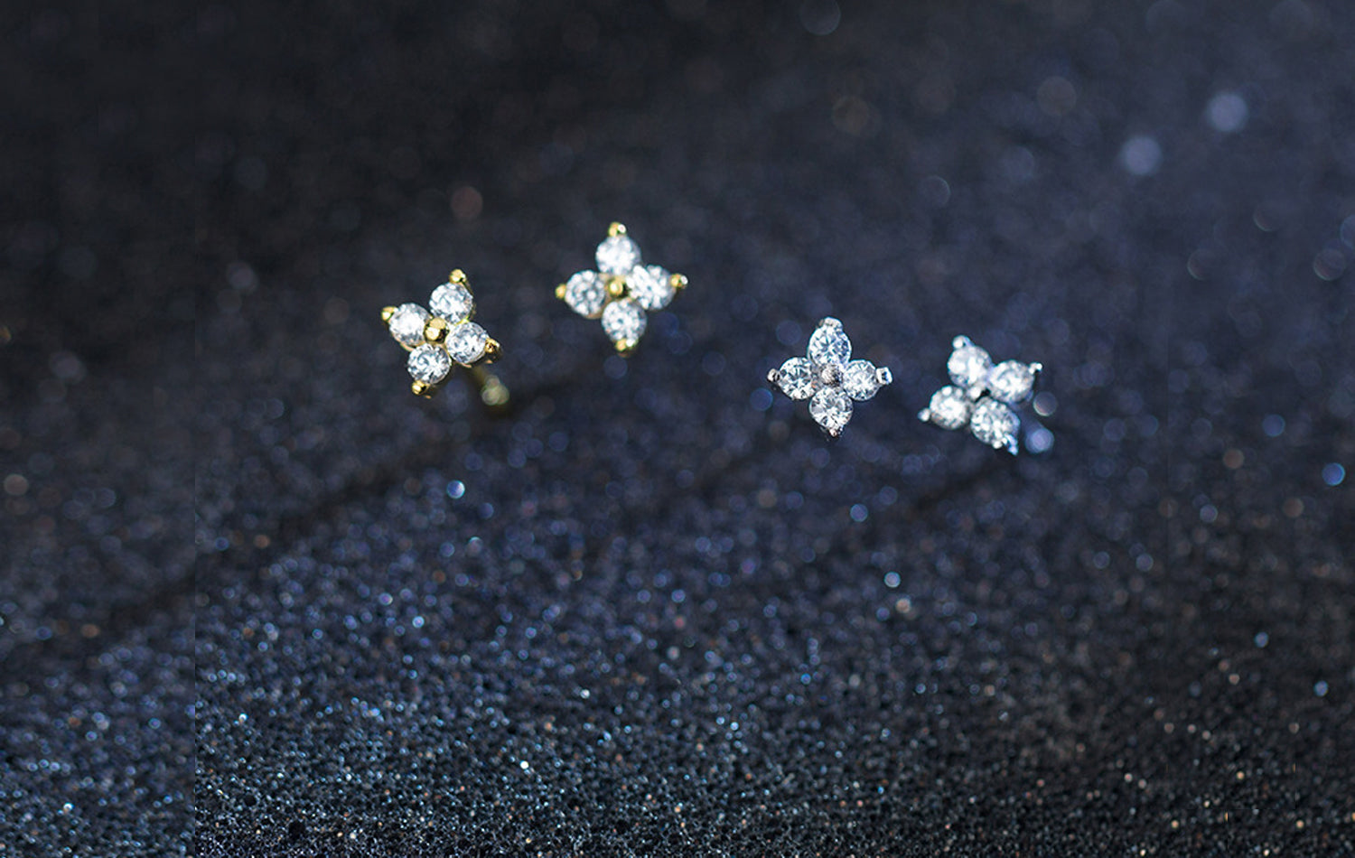 Four diamond stud earrings on a dark textured surface