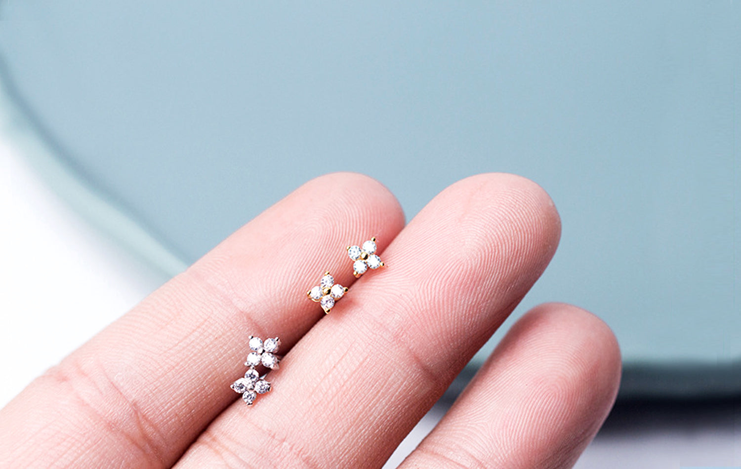 Silver floral earrings on a hand with a light blue background