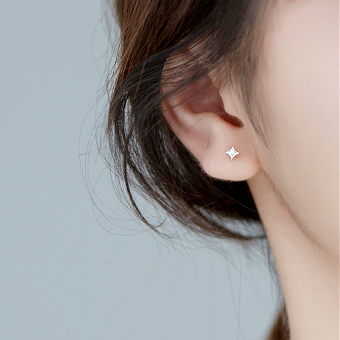 Close-up of an ear wearing a diamond-shaped earring against a plain background