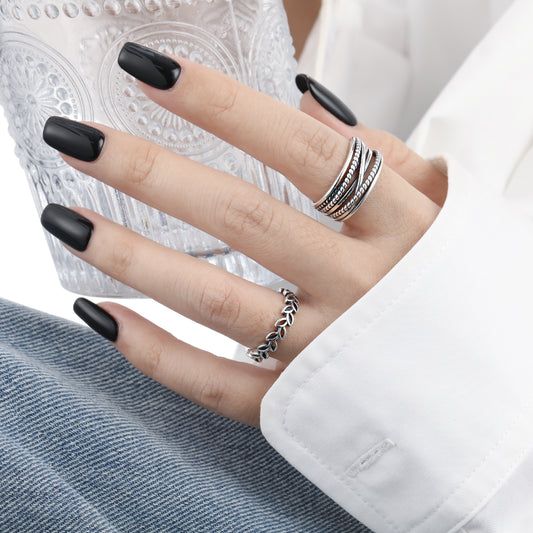 Hand with black nail polish wearing multiple rings on a blurred background