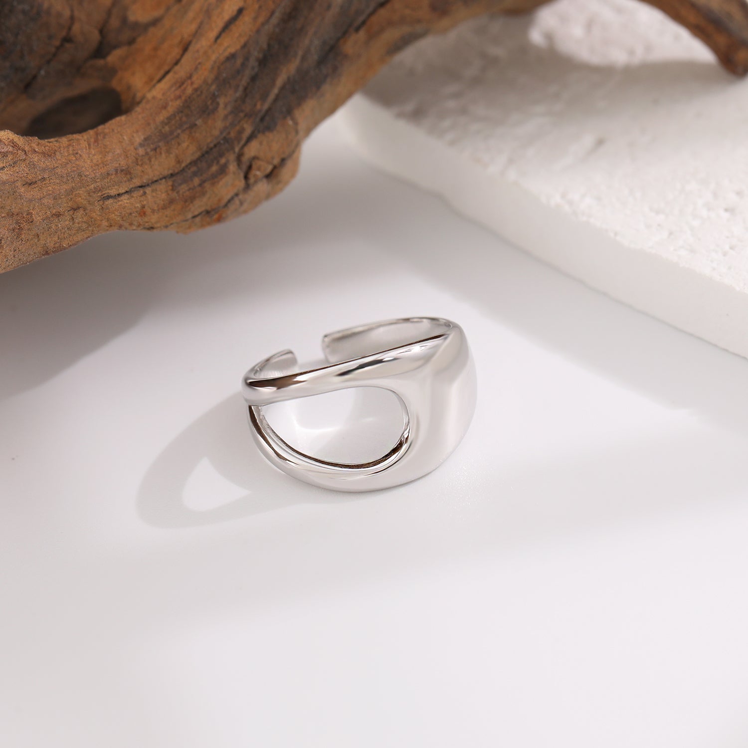 Silver ring on a white surface with a natural wood piece in the background