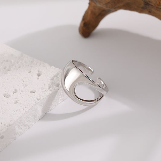 Silver ring on a textured white surface with a wooden object in the background