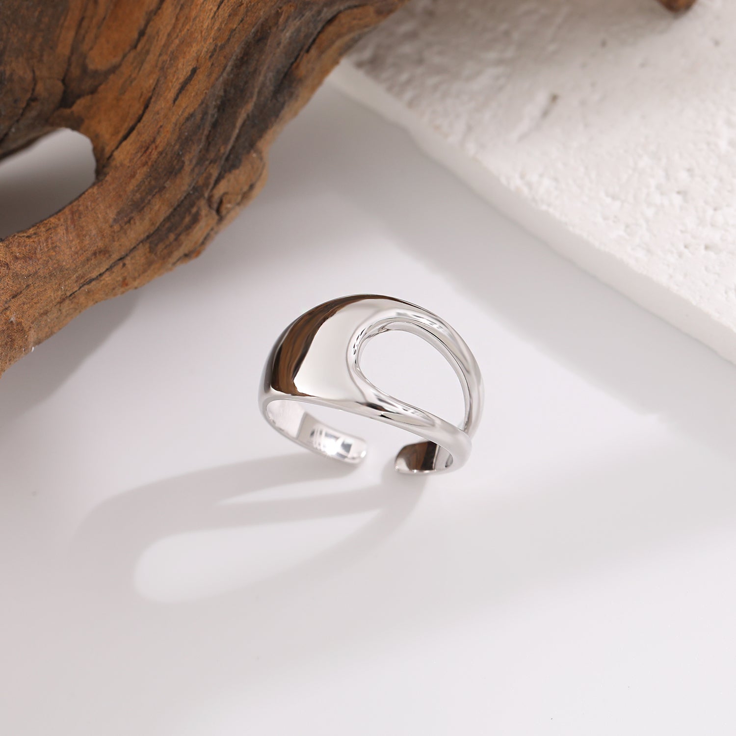 Silver ring on a white surface with a natural wood and stone background