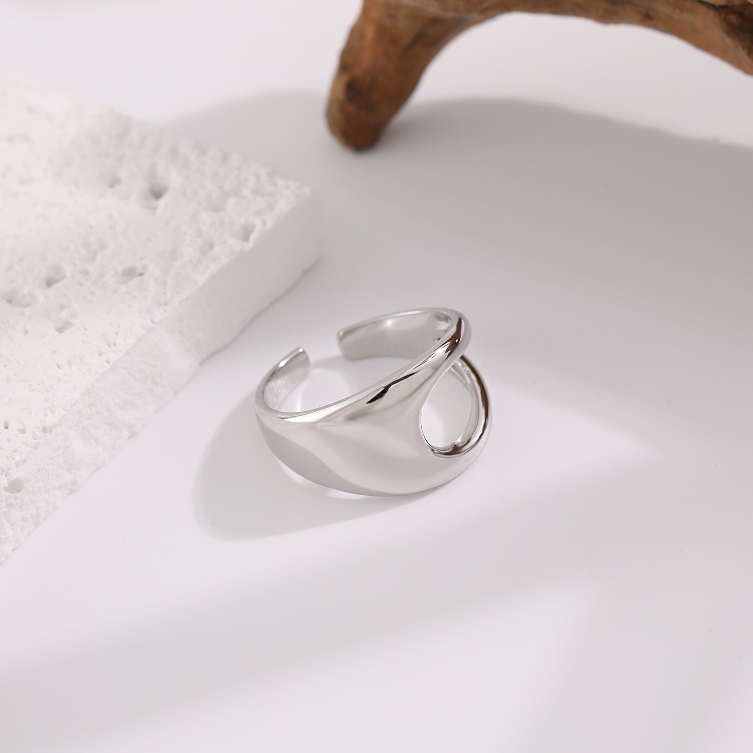 Silver ring on a white surface with a natural wood piece in the background