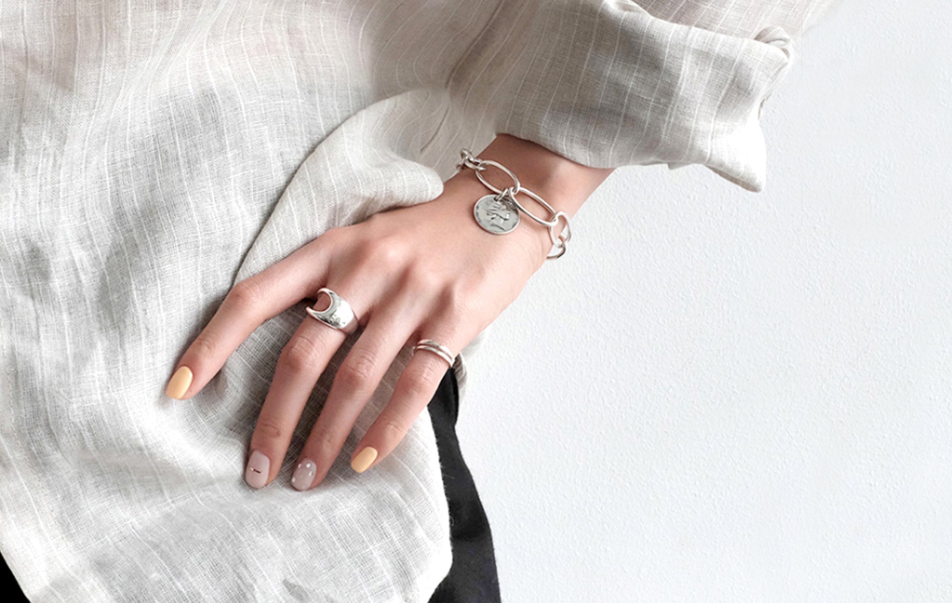 Hand wearing multiple silver rings on a light background