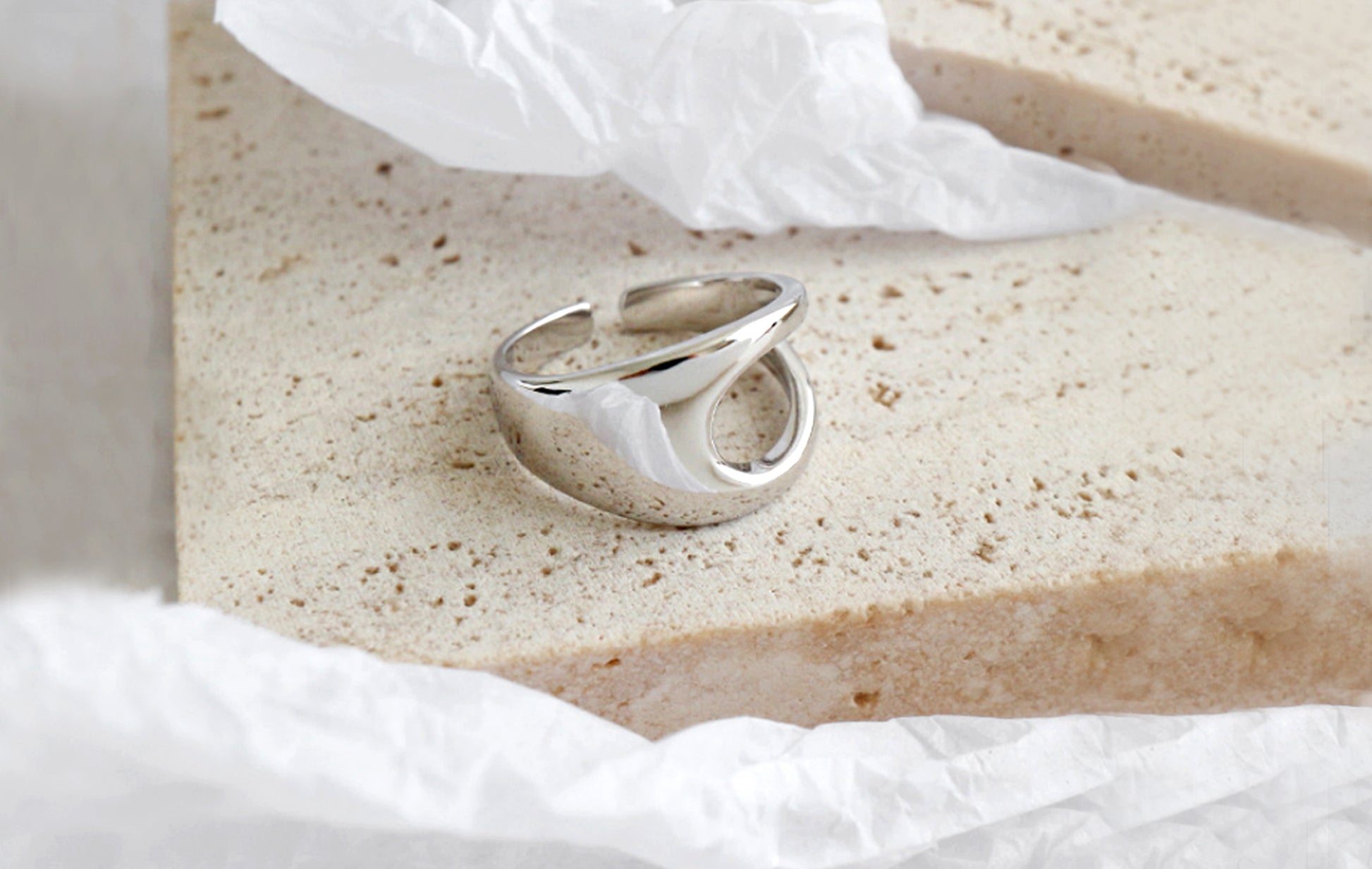 Silver ring on a textured beige surface with white tissue paper