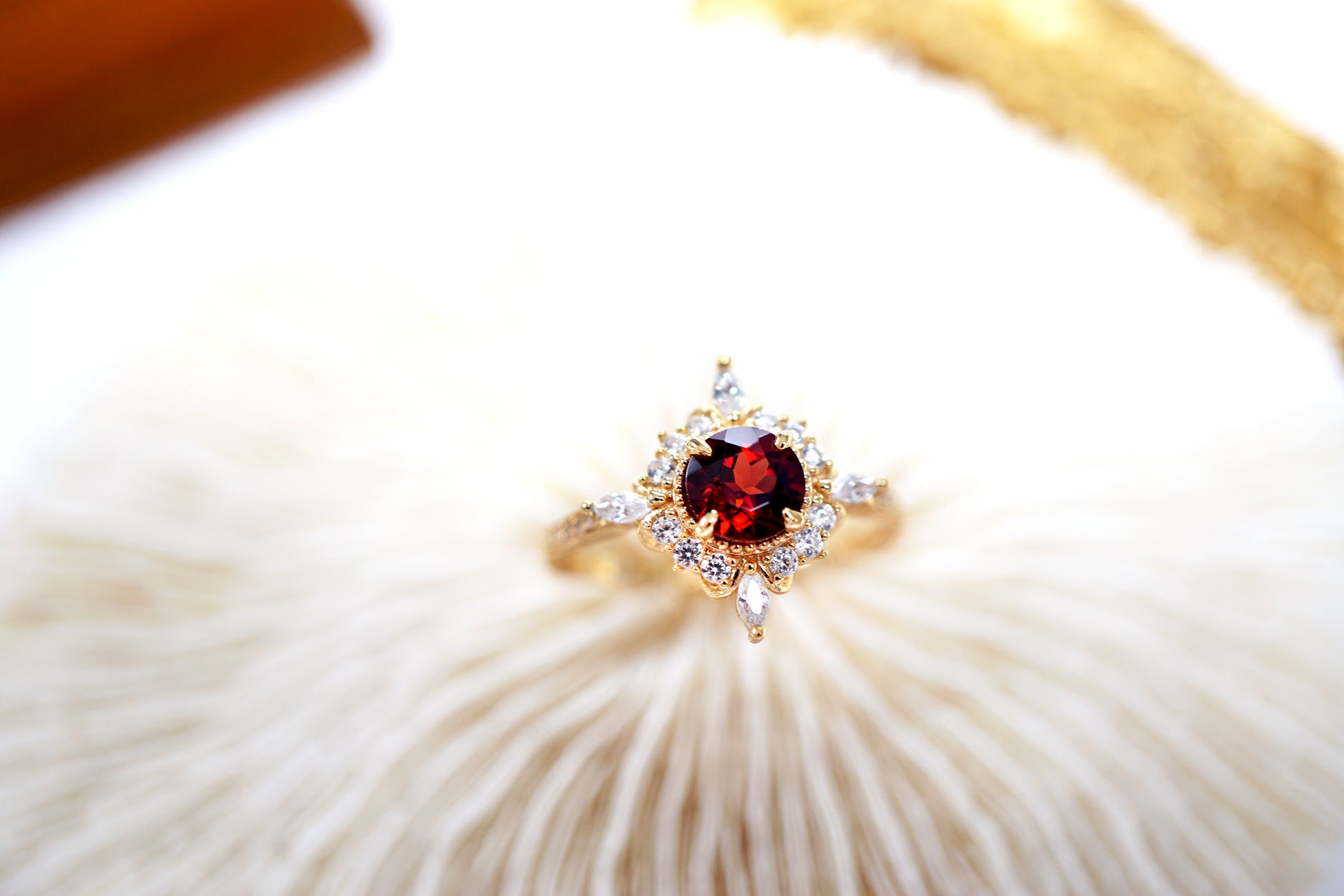 Gold ring with a red gemstone on a white shell background