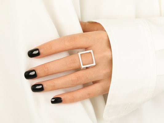 Hand wearing a square ring with black nail polish on a white background