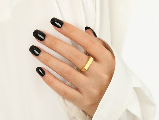 Hand with black nail polish wearing a gold ring on a white background