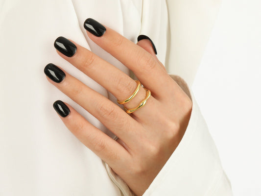 Hand with black nail polish and gold rings on a white background