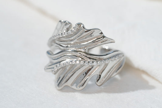 Silver ring with leaf design on a light wooden surface