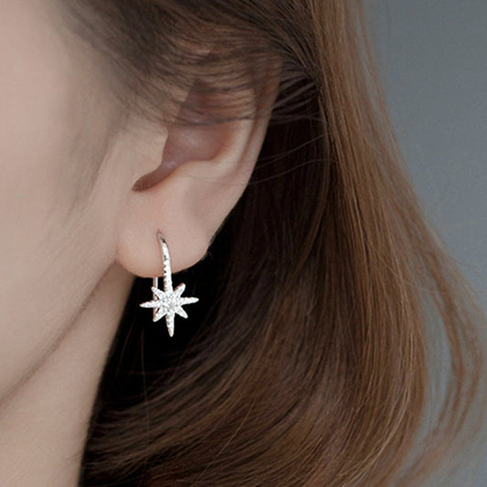 Close-up of a person wearing a silver star-shaped earring against a neutral background